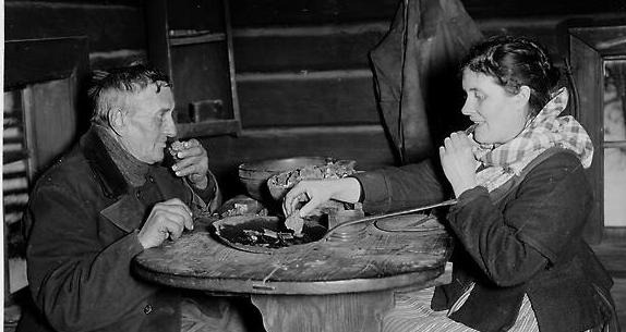 svartvitt fotografi med äldre par som sitter mitt emot varandra vid ett bord och äter