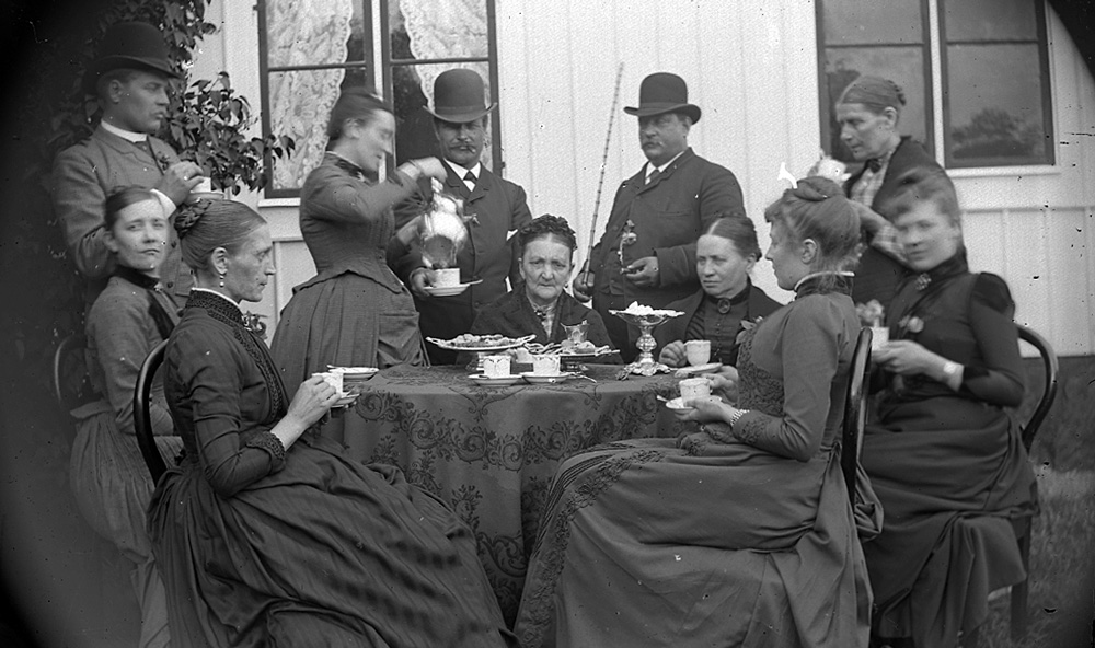 svartvitt fotografi med finklädda män och kvinnor runt ett kaffebord